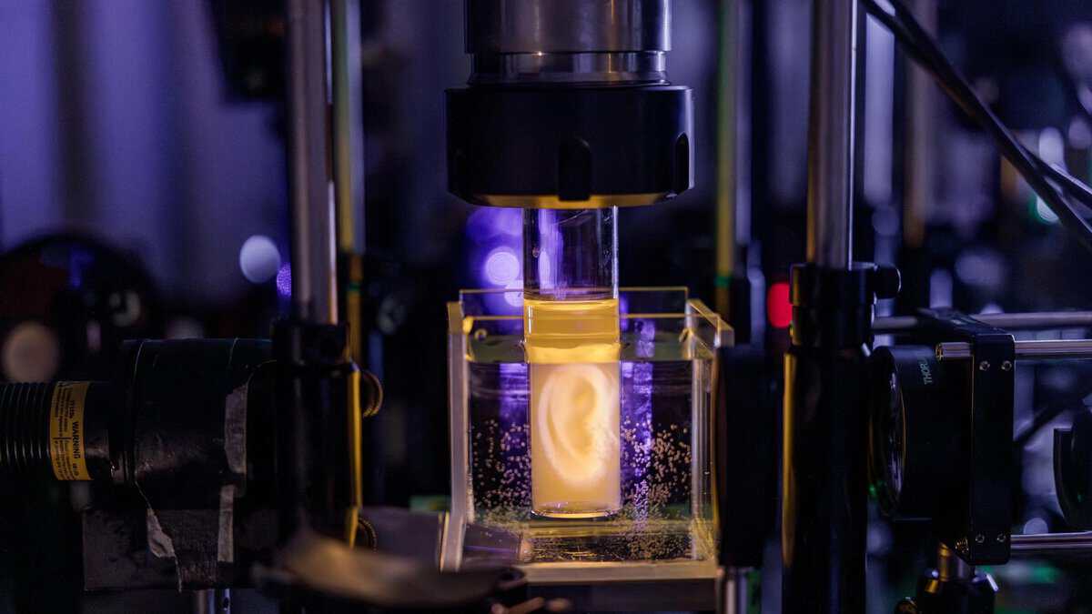 EPFL's holographic volumetric 3D printing platform with a life-sized human ear forming inside a resin-filled vial illuminated by laser light in the Laboratory of Applied Photonic Devices